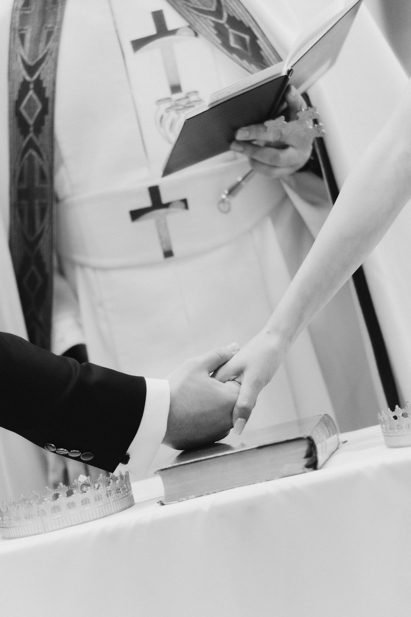 Black and white close-up of hands holding a Bible with stefana crowns at St Michael's Catholic Church Baulkham Hills
