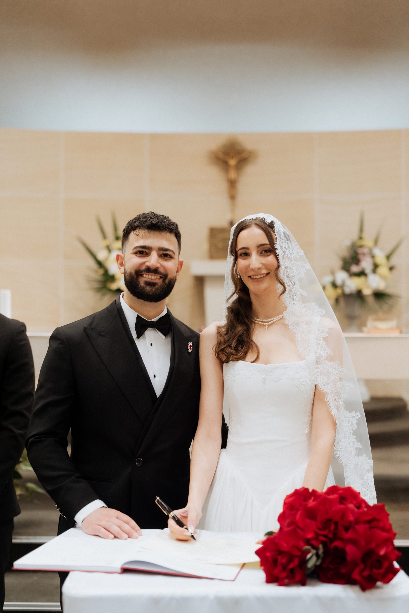 Ashleigh and Morry signing the wedding register at St Michael's Catholic Church surrounded by red roses
